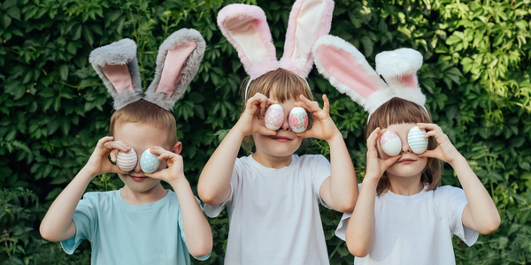 Drie kinderen met konijnenoortjes houden paaseitjes voor hun ogen.